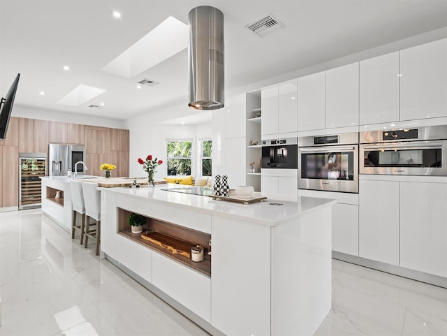 kitchen featuring stainless steel appliances, light countertops, a large island with sink, and white cabinets