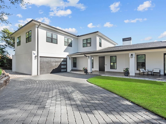 view of front of house with an attached garage, decorative driveway, stucco siding, a chimney, and a front yard