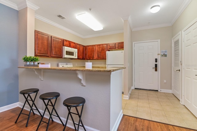 kitchen featuring a peninsula, white appliances, visible vents, light wood finished floors, and a kitchen bar