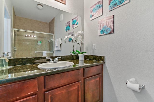 full bath with a textured wall, a shower stall, and vanity