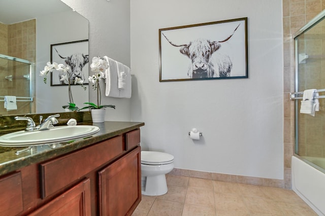 bathroom with baseboards, toilet, shower / bath combination with glass door, tile patterned flooring, and vanity