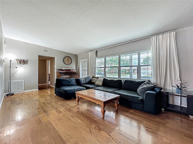 living room with light hardwood / wood-style flooring, vaulted ceiling, and a textured ceiling