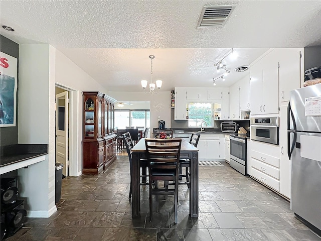 kitchen with hanging light fixtures, stainless steel appliances, a textured ceiling, white cabinets, and a chandelier