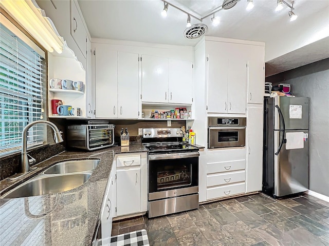 kitchen with dark stone countertops, white cabinetry, stainless steel appliances, and sink