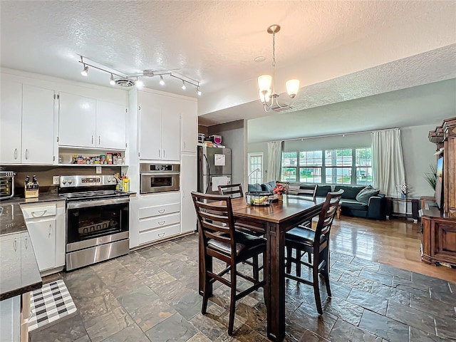 kitchen featuring hanging light fixtures, a textured ceiling, appliances with stainless steel finishes, white cabinets, and a chandelier