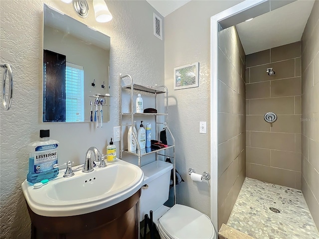 bathroom with a tile shower, vanity, and toilet