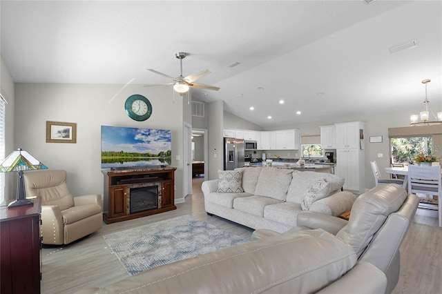 living area with light wood-type flooring, ceiling fan with notable chandelier, and a glass covered fireplace