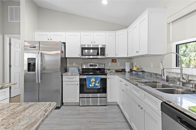 kitchen with appliances with stainless steel finishes, white cabinets, a sink, and light stone countertops