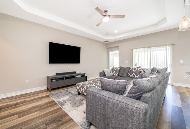 living room with wood-type flooring, ceiling fan, and a tray ceiling