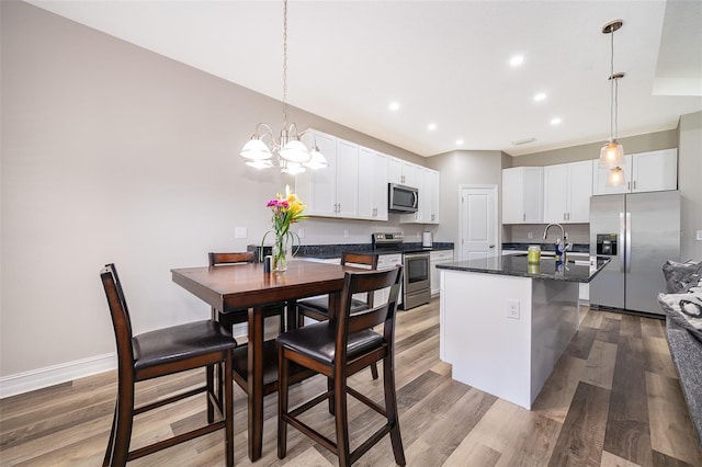 kitchen with appliances with stainless steel finishes, a center island with sink, hanging light fixtures, white cabinets, and hardwood / wood-style floors