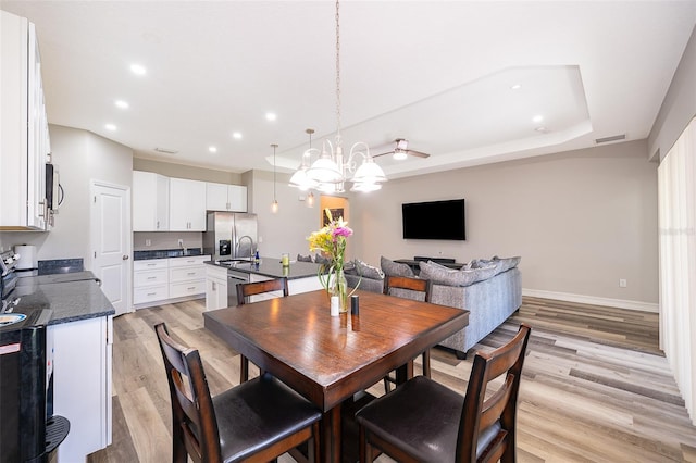 dining space with a tray ceiling, an inviting chandelier, and light hardwood / wood-style floors