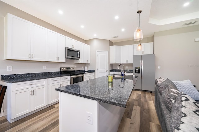kitchen with white cabinets, an island with sink, stainless steel appliances, and decorative light fixtures