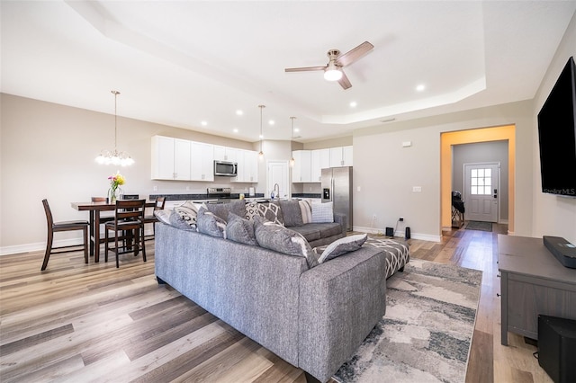 living room featuring ceiling fan with notable chandelier, light hardwood / wood-style floors, and a raised ceiling
