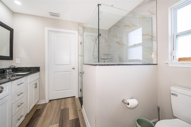 bathroom with toilet, vanity, tiled shower, and wood-type flooring