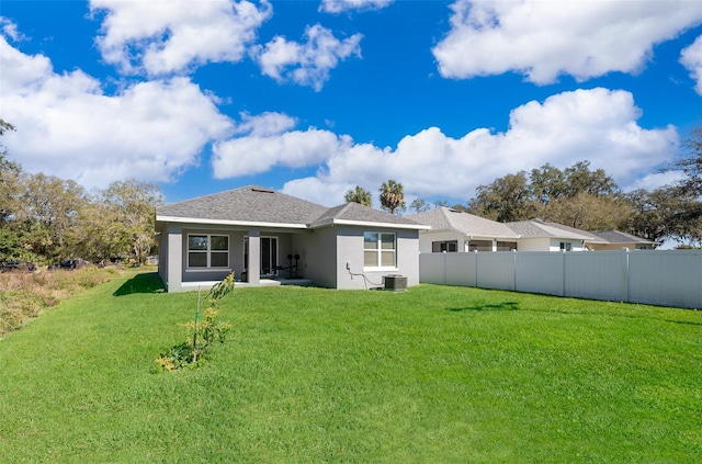 rear view of property with central AC unit and a yard