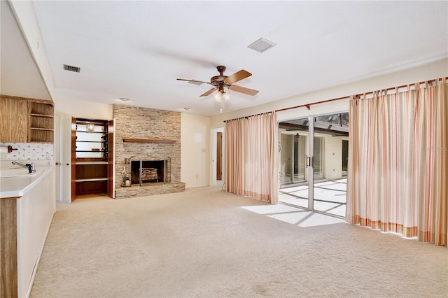 unfurnished living room with sink, a brick fireplace, light colored carpet, and ceiling fan