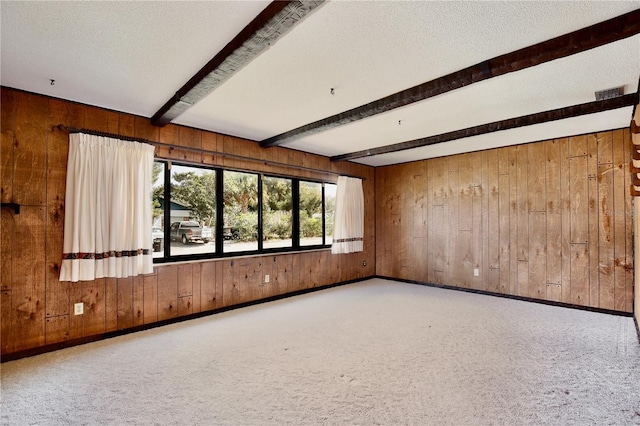 empty room featuring wood walls, beamed ceiling, carpet flooring, and a textured ceiling