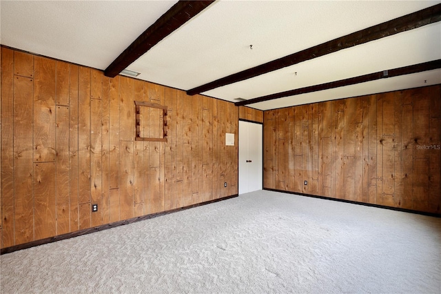 unfurnished room featuring beamed ceiling, light carpet, a textured ceiling, and wooden walls