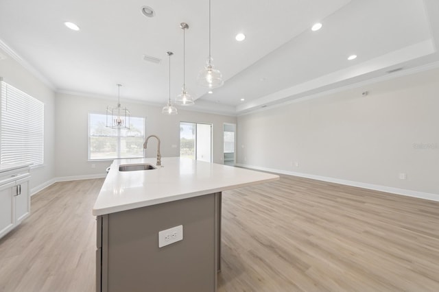 kitchen with a sink, a kitchen island with sink, light wood-type flooring, baseboards, and ornamental molding