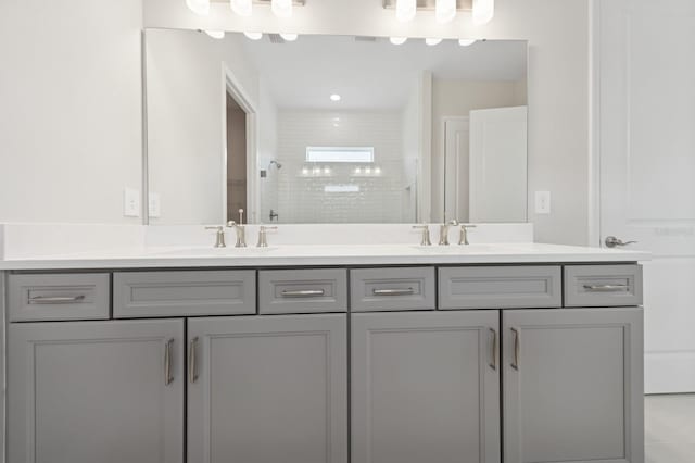 full bath featuring double vanity, tiled shower, and a sink