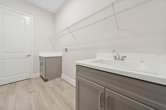 washroom featuring a sink, cabinet space, light wood finished floors, washer hookup, and baseboards