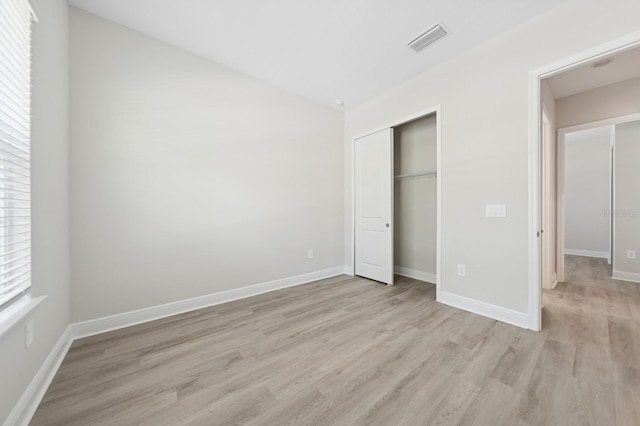 unfurnished bedroom with a closet, baseboards, visible vents, vaulted ceiling, and light wood-type flooring