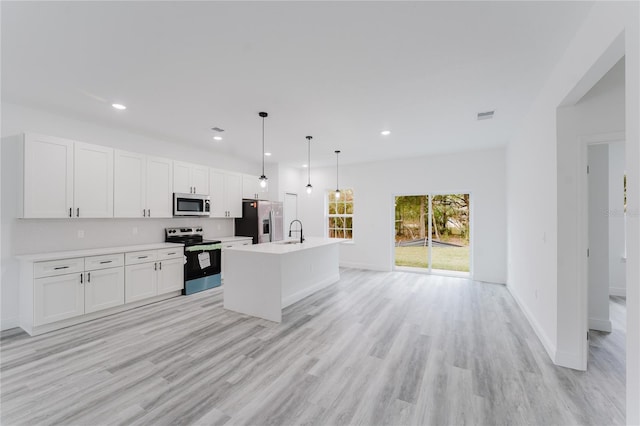 kitchen with stainless steel appliances, light countertops, white cabinets, a sink, and an island with sink