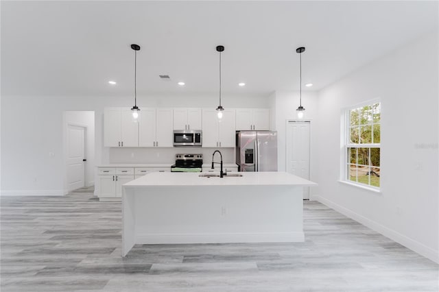 kitchen with stainless steel appliances, a kitchen island with sink, white cabinetry, and a sink