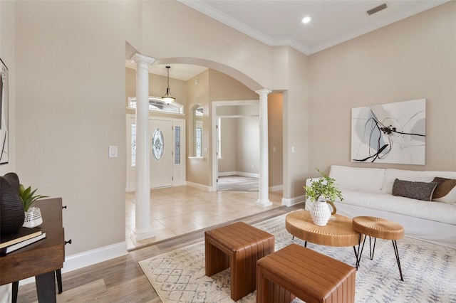 living room with arched walkways, visible vents, light wood-style flooring, ornamental molding, and ornate columns