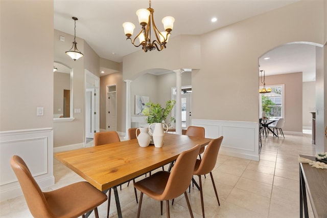 dining area with light tile patterned floors, arched walkways, a wainscoted wall, ornate columns, and a decorative wall