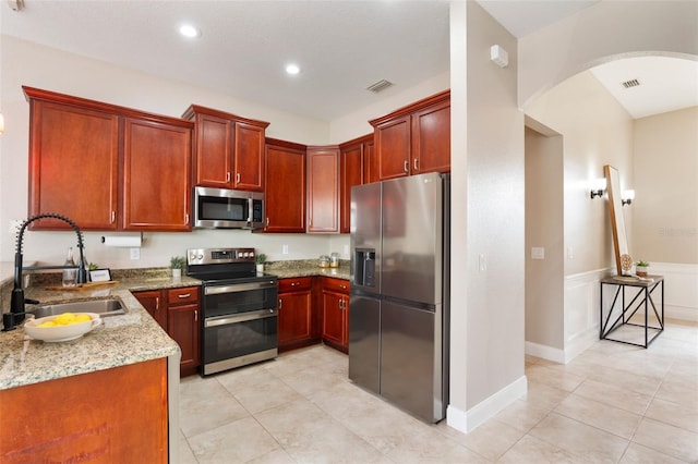 kitchen with visible vents, arched walkways, light stone countertops, stainless steel appliances, and a sink