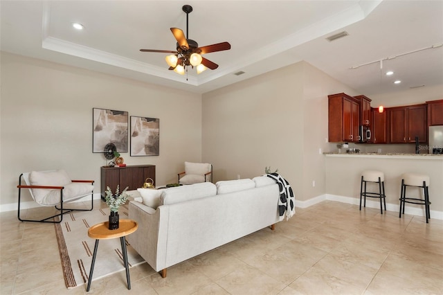 living room with a tray ceiling, visible vents, and baseboards