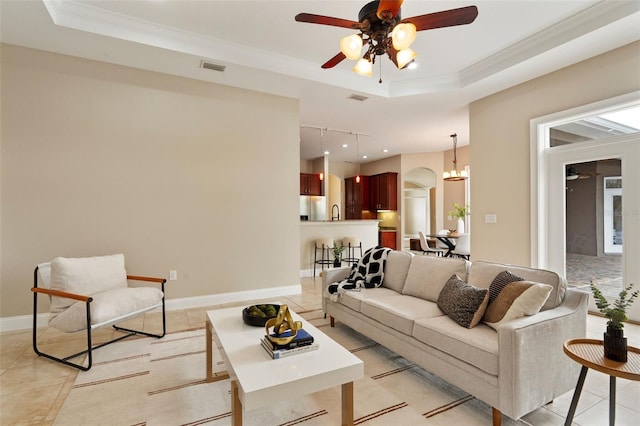 living area with baseboards, visible vents, arched walkways, a tray ceiling, and crown molding