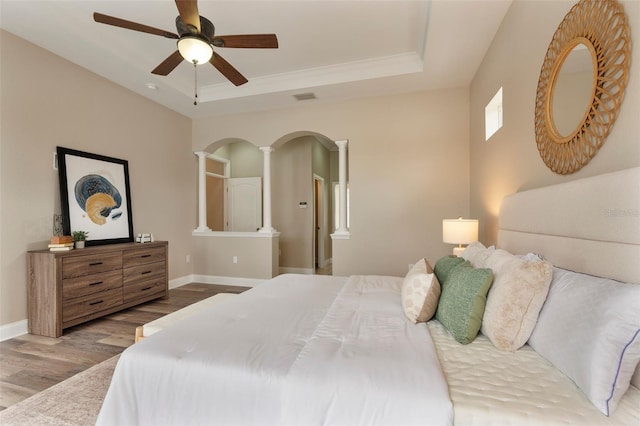 bedroom featuring a tray ceiling, arched walkways, visible vents, wood finished floors, and baseboards