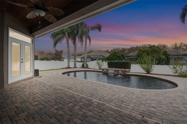 pool at dusk with a ceiling fan, a patio, a fenced backyard, french doors, and a pool with connected hot tub