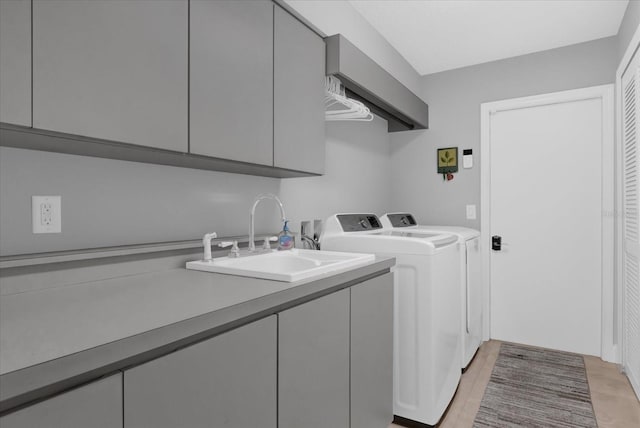 clothes washing area with cabinet space, washer and dryer, and a sink