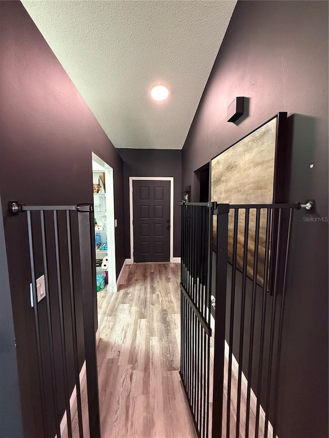 corridor featuring lofted ceiling, a textured ceiling, and light wood finished floors