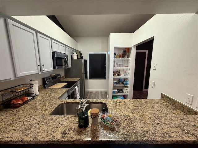 kitchen with stainless steel appliances, a peninsula, a sink, white cabinets, and dark stone countertops