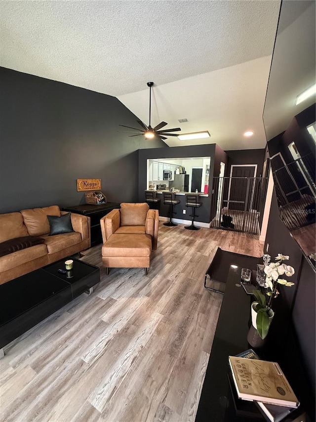 living room with lofted ceiling, visible vents, ceiling fan, a textured ceiling, and light wood-type flooring