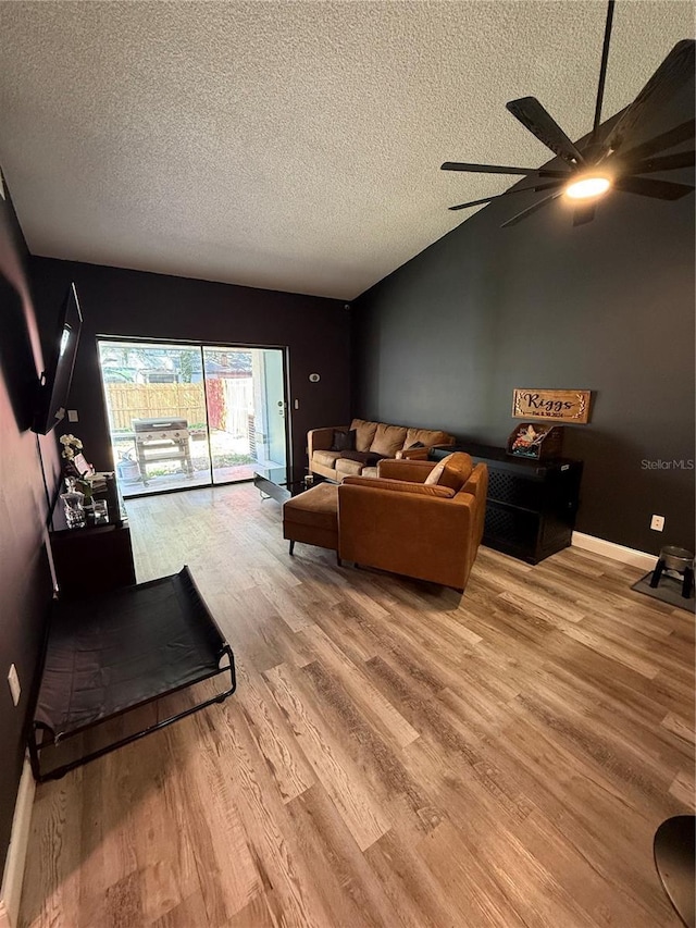 living room with ceiling fan, a textured ceiling, baseboards, vaulted ceiling, and light wood finished floors