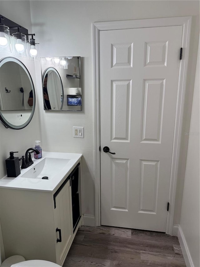 half bath featuring vanity, baseboards, and wood finished floors