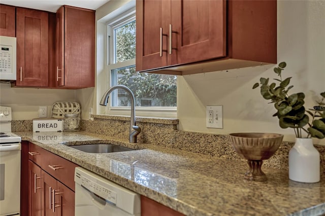 kitchen with light stone counters, white appliances, a sink, and dark brown cabinets