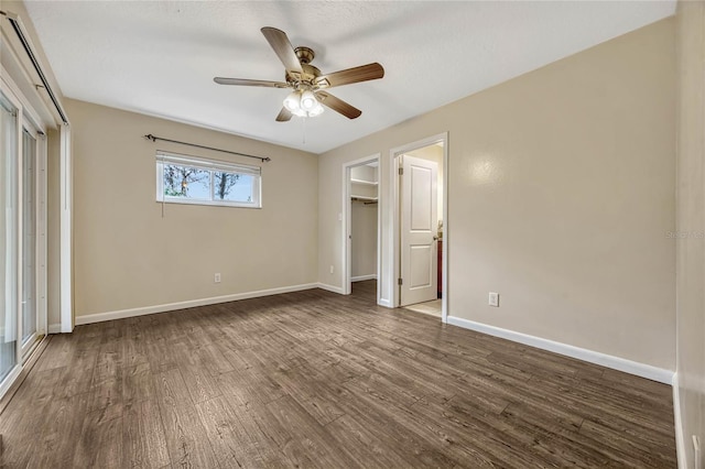 unfurnished bedroom featuring a ceiling fan, baseboards, a walk in closet, and wood finished floors