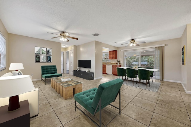 living room featuring light tile patterned floors, visible vents, baseboards, ceiling fan, and a textured ceiling