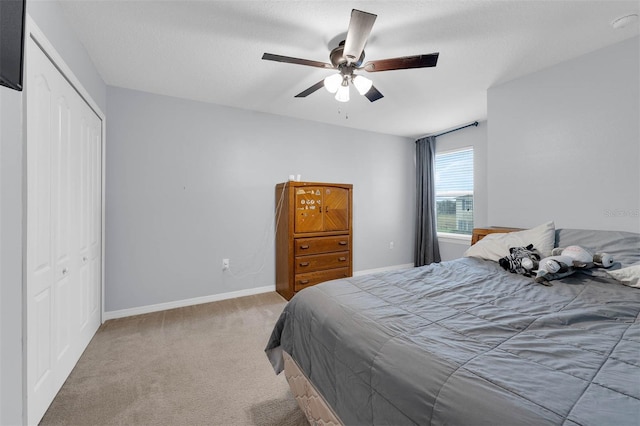 bedroom featuring a closet, light carpet, ceiling fan, a textured ceiling, and baseboards