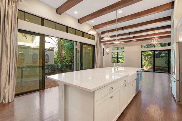 kitchen featuring an island with sink, light stone countertops, white cabinets, pendant lighting, and stainless steel refrigerator