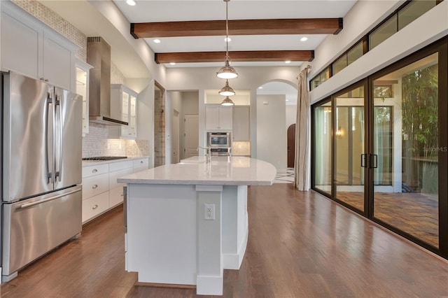 kitchen with white cabinetry, an island with sink, stainless steel refrigerator, wall chimney exhaust hood, and pendant lighting