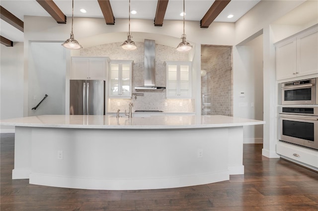 kitchen with hanging light fixtures, wall chimney exhaust hood, stainless steel appliances, a spacious island, and white cabinetry