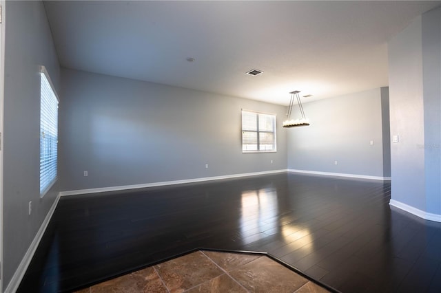 empty room featuring dark wood-style floors, visible vents, and baseboards