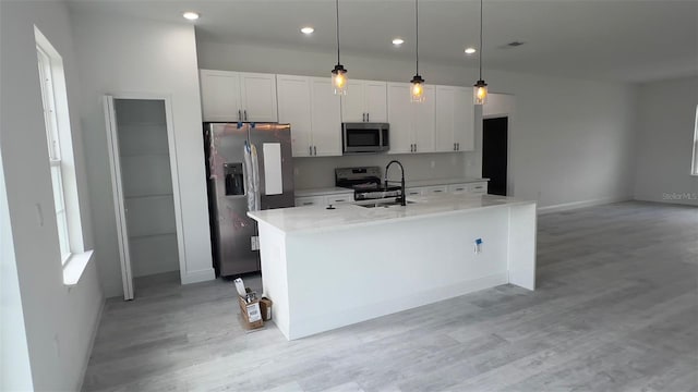 kitchen with an island with sink, white cabinetry, stainless steel appliances, decorative light fixtures, and sink